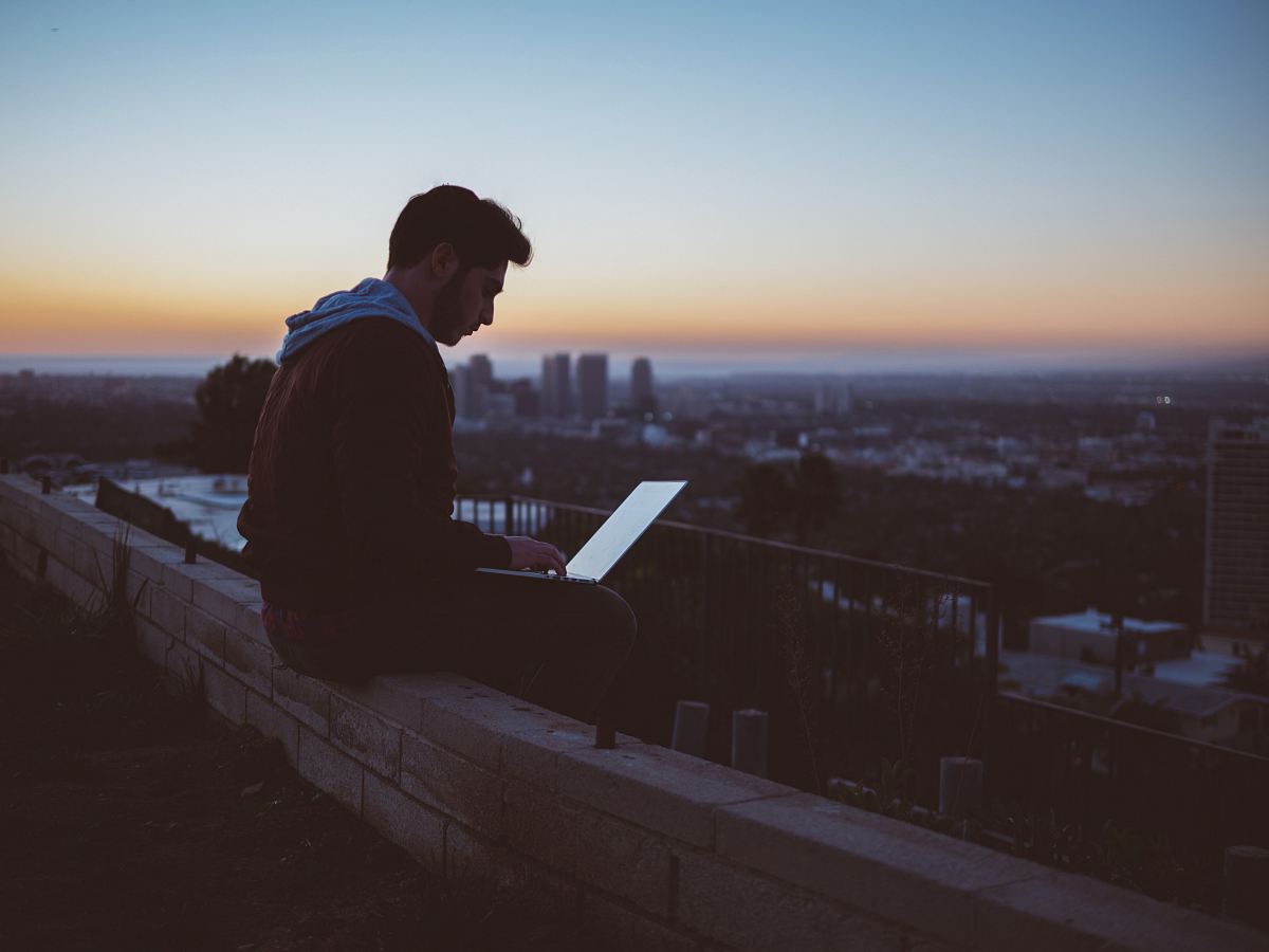 man sitting on concrete brick with opened laptop on his lap