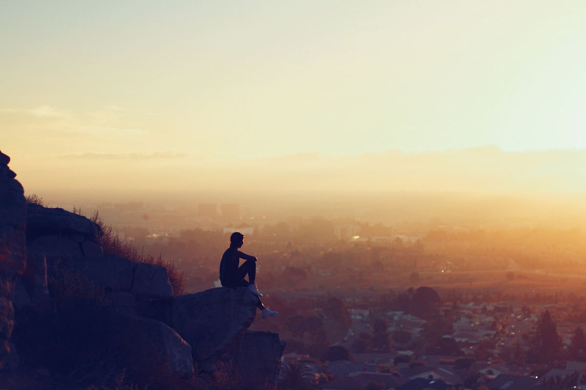 man sitting on rock formation in cliff during golden hours