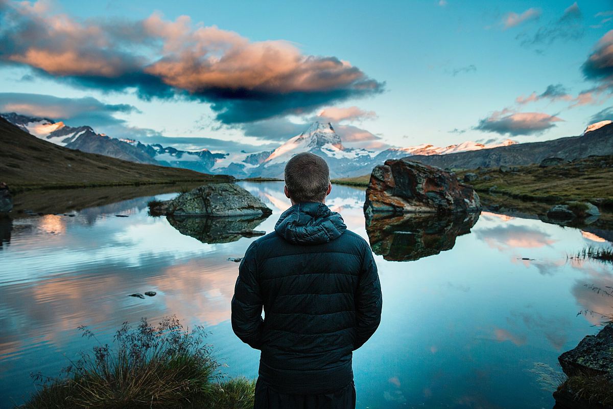 man standing in front view of lake surrounded with mountains