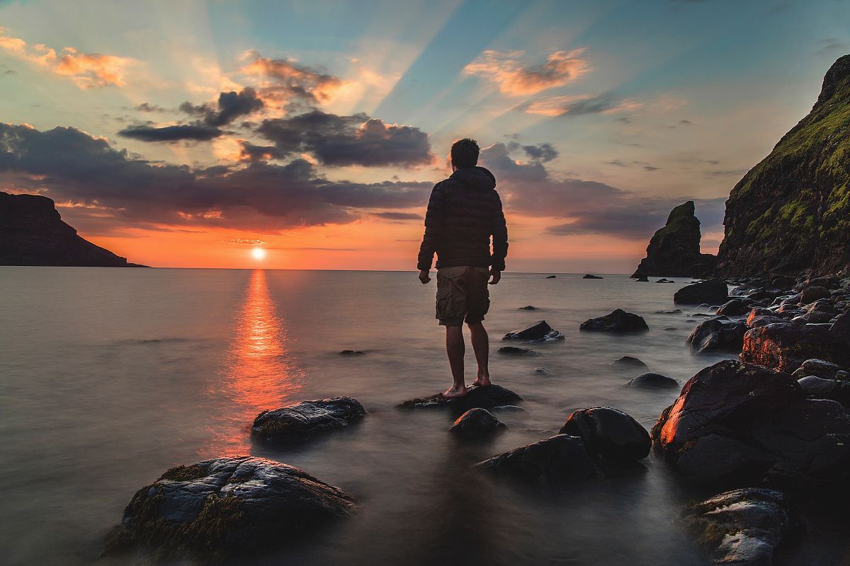 man standing on stone looking at sunset