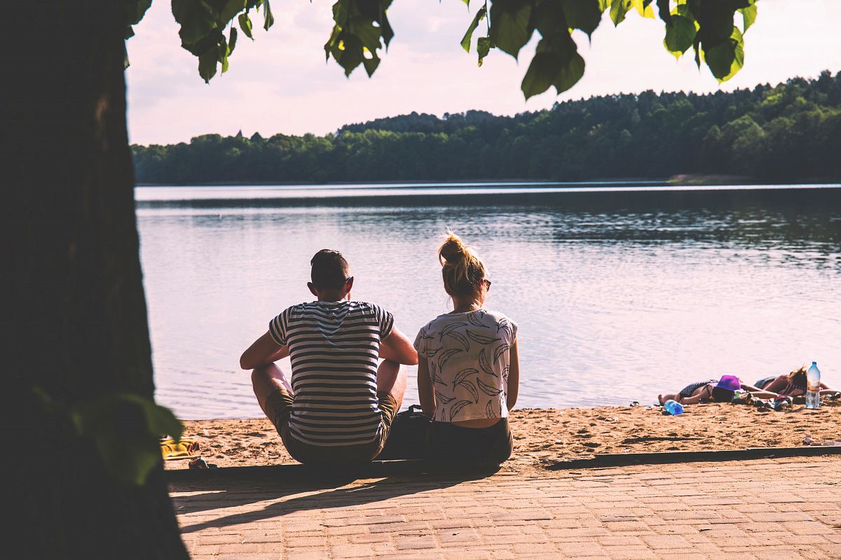 men and woman sitting on pavement facing body of water