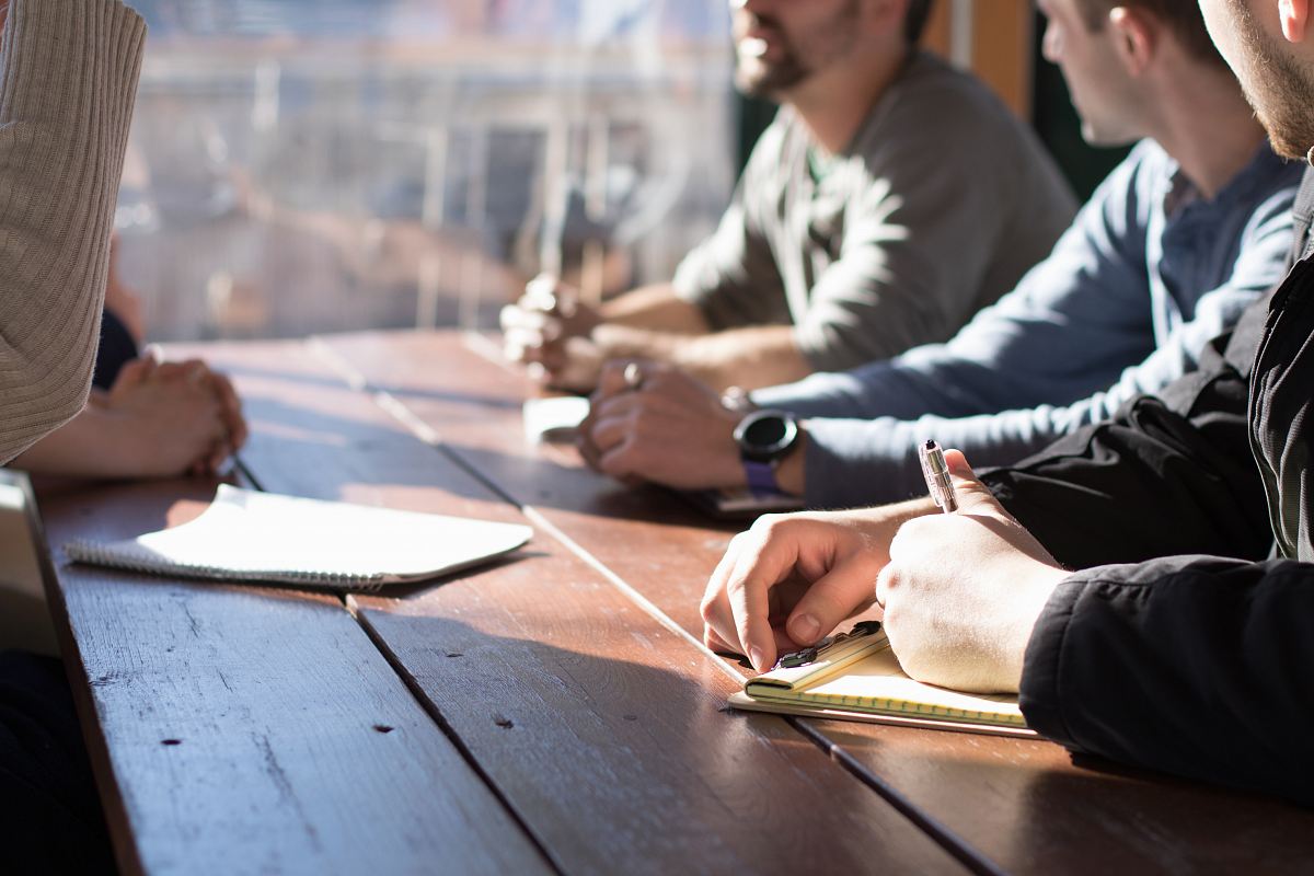 people sitting on chair in front of table while holding pens during daytime