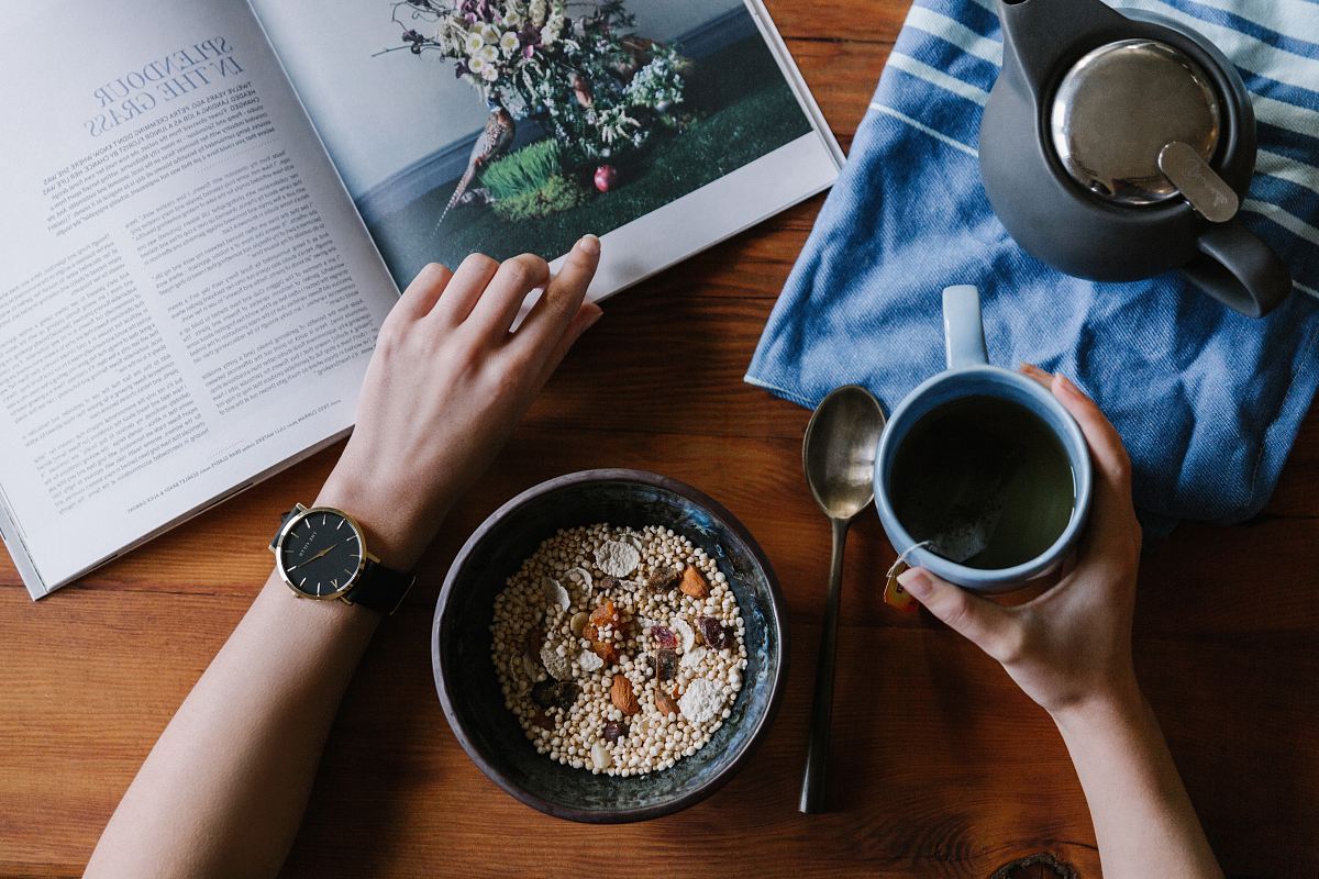 person holding blue ceramic mug and white magazine
