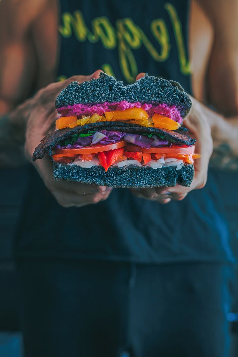 person holding meat sandwich with sliced tomatoes, onions, and grilled meat