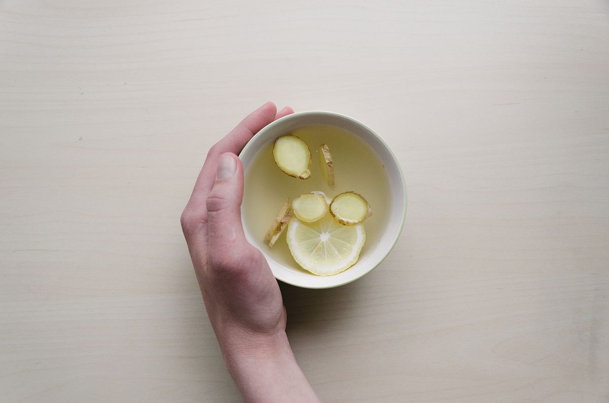 person holding white bowl with sliced lime and ginger inside