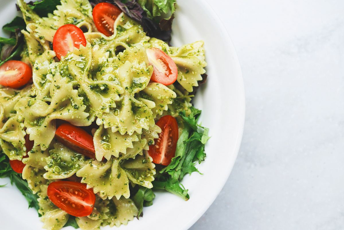 Pesto pasta with sliced tomatoes served on white ceramic plate