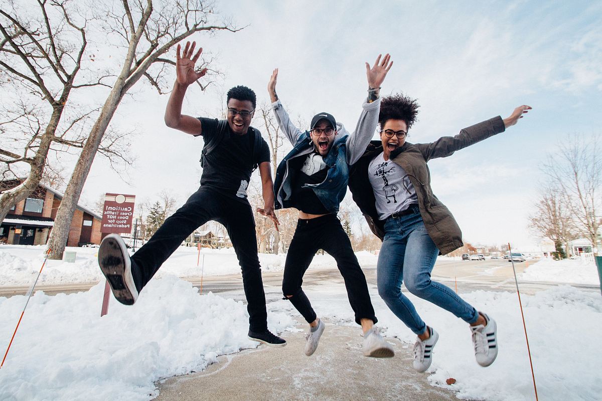 photo of three men jumping on ground near bare trees during daytime