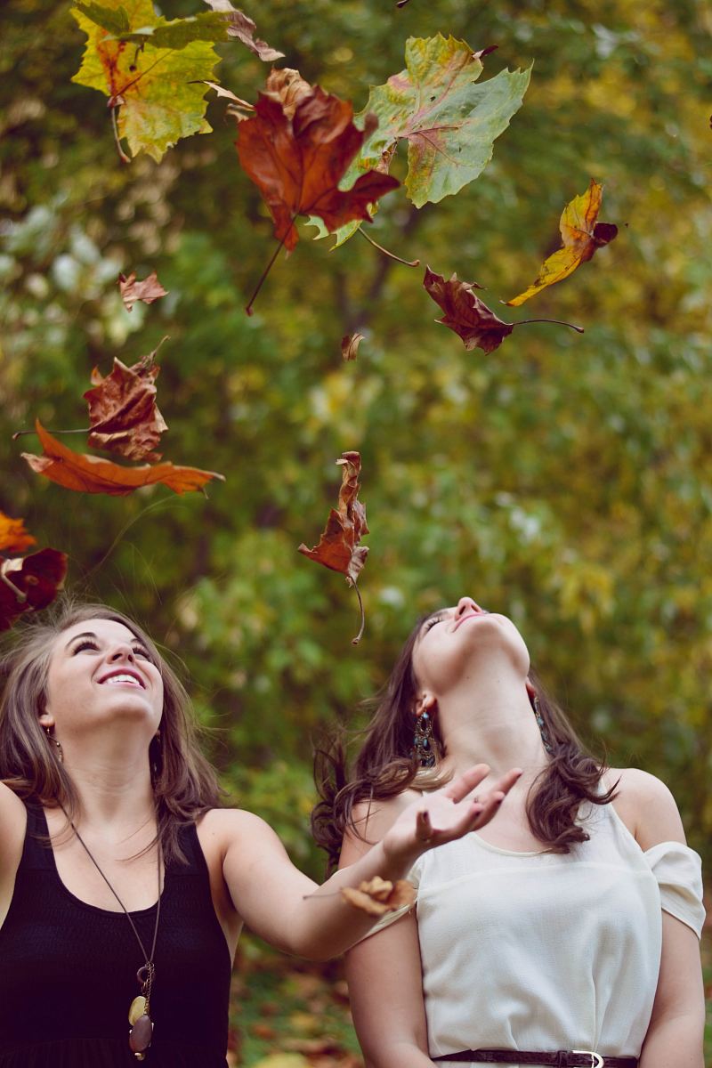 photo of two women throwing leaves during daytime