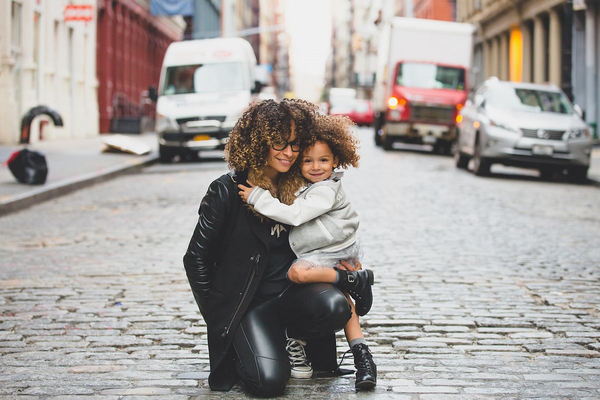 photography of woman carrying baby near street during daytime