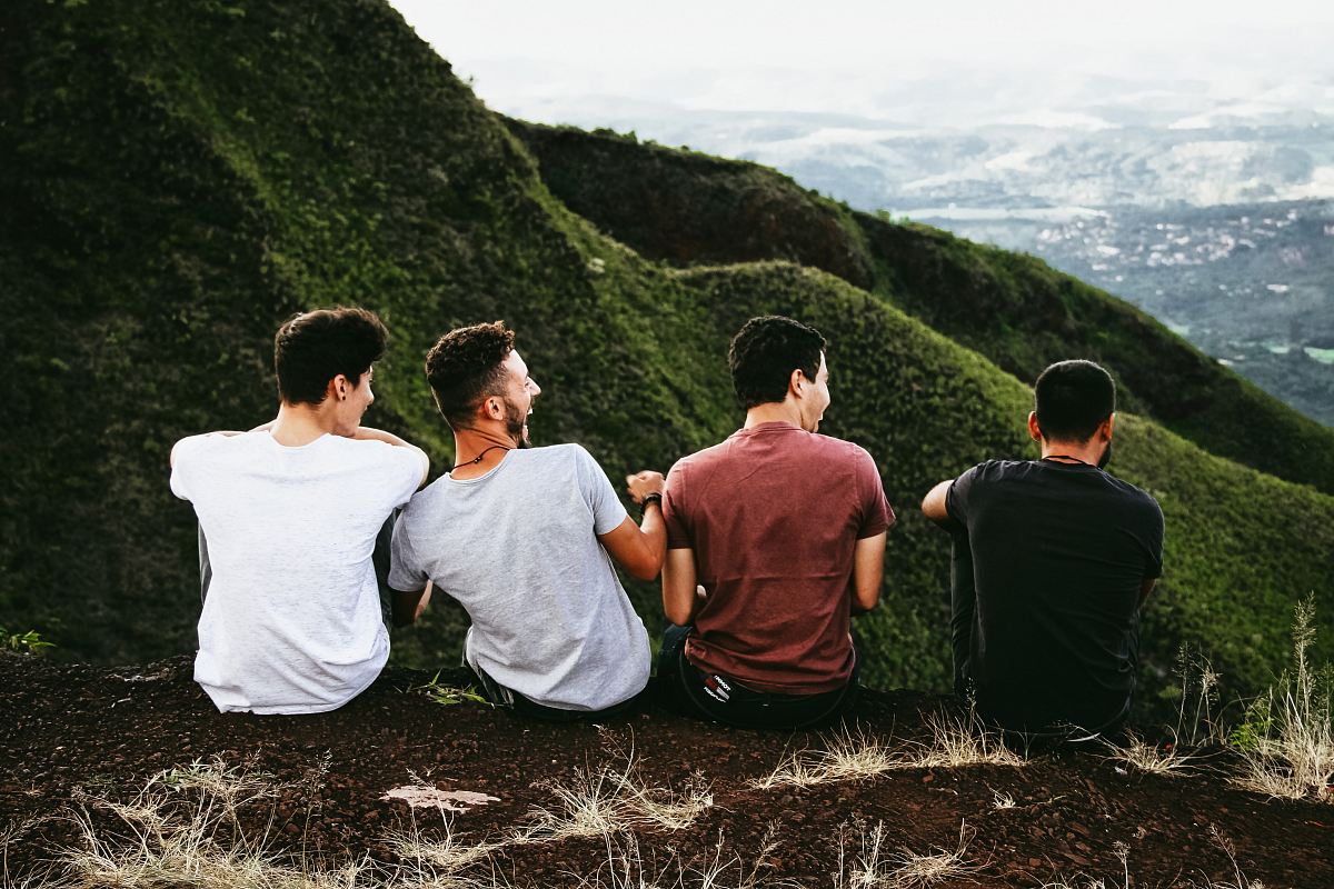row of four men sitting on mountain trail