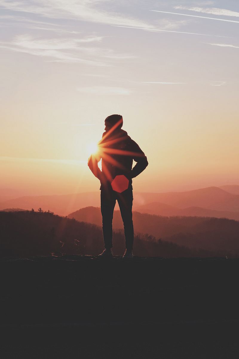 silhouette of man standing near cliff in golden hour background
