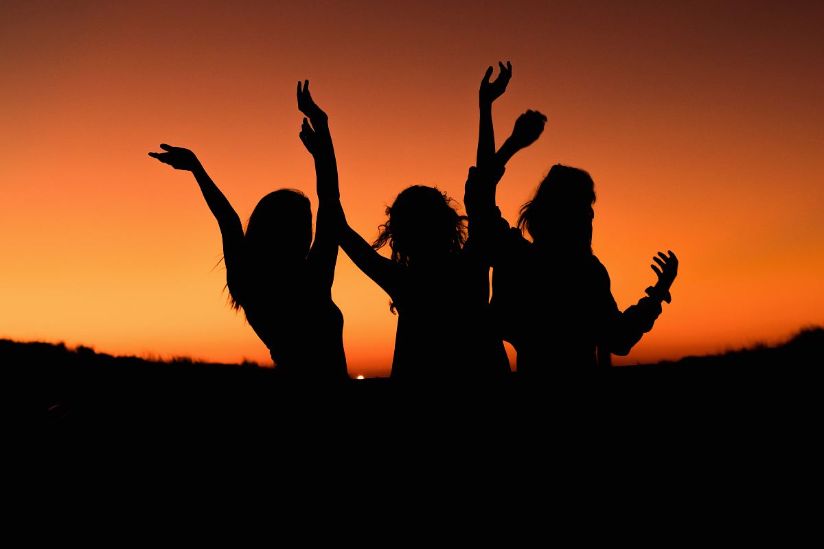silhouette of three woman with hands on the air while dancing during sunset