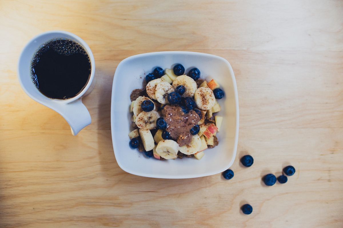 sliced bananas with berries and peanut butter beside cup of coffee on table