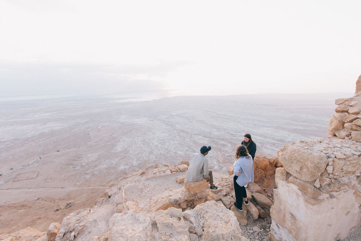 three person on cliff under white sky