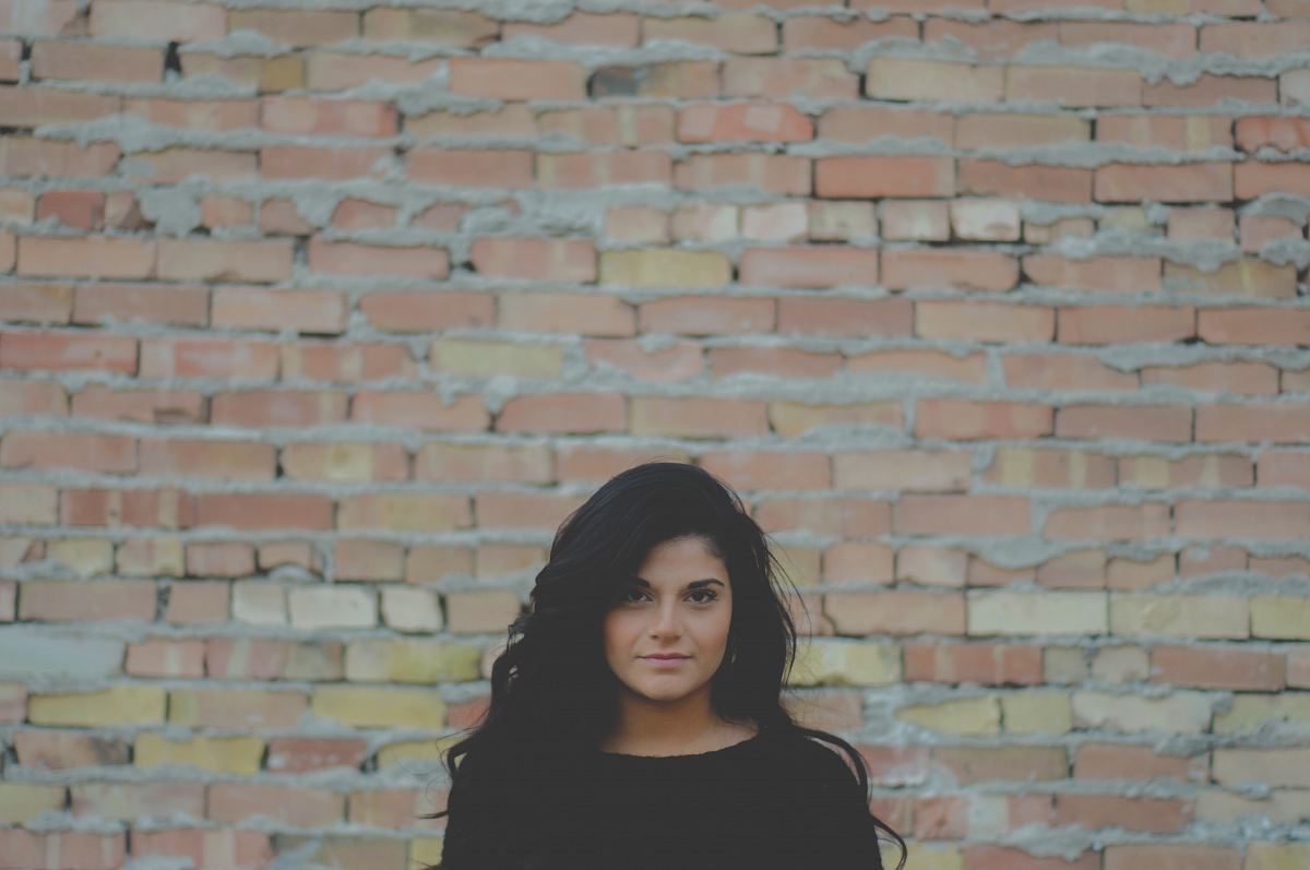 tilt shift lens photography of woman standing near brown brick wall