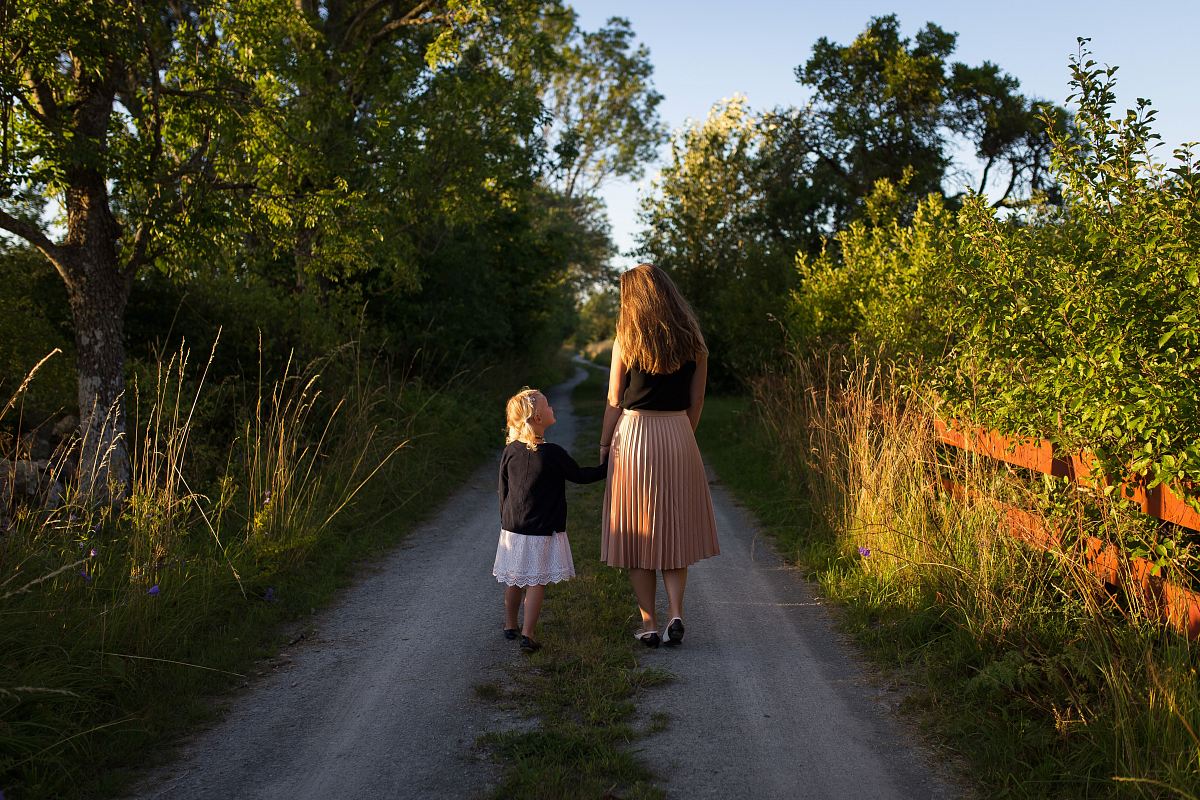 woman and girl walking on road surrounded by green grass