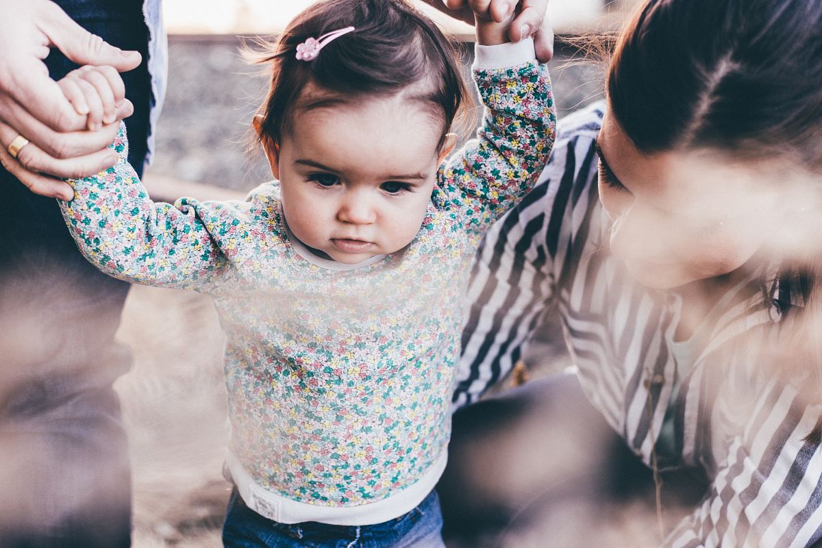 woman holding girl while learning to walk taken at daytime