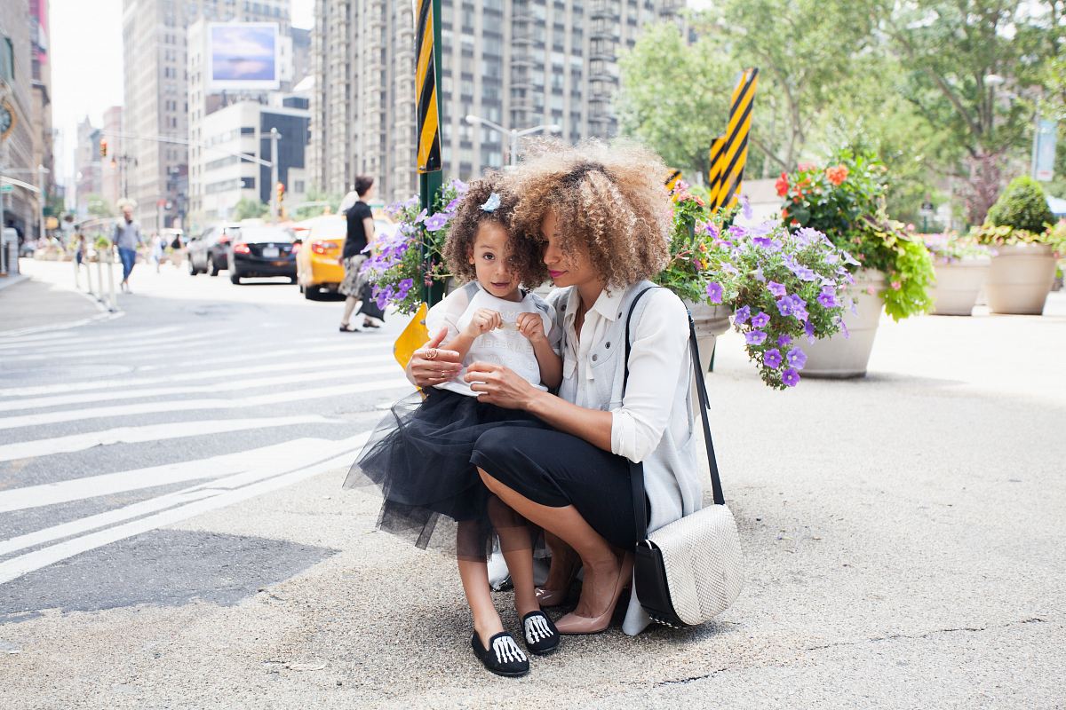 woman in white dress shirt holding her daughter in tutu dress beside of asphalt road during daytime