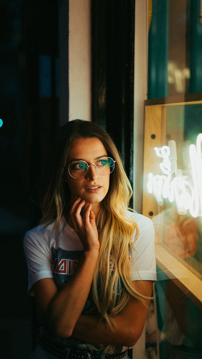 woman leaning on white wall with eyeglasses taking photo inside dark room