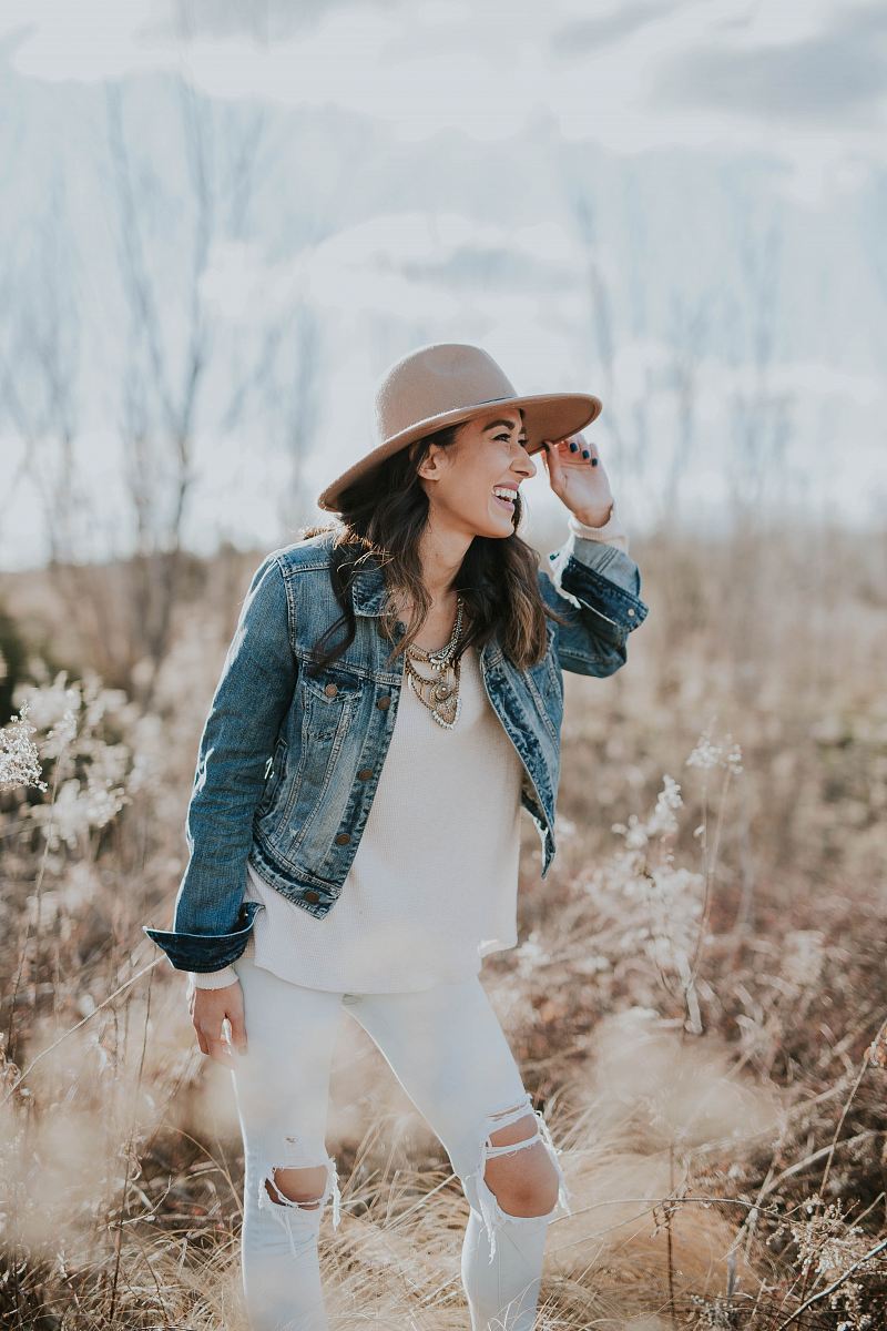 woman standing on dried grass facing right while holding her brown sun hat during daytime