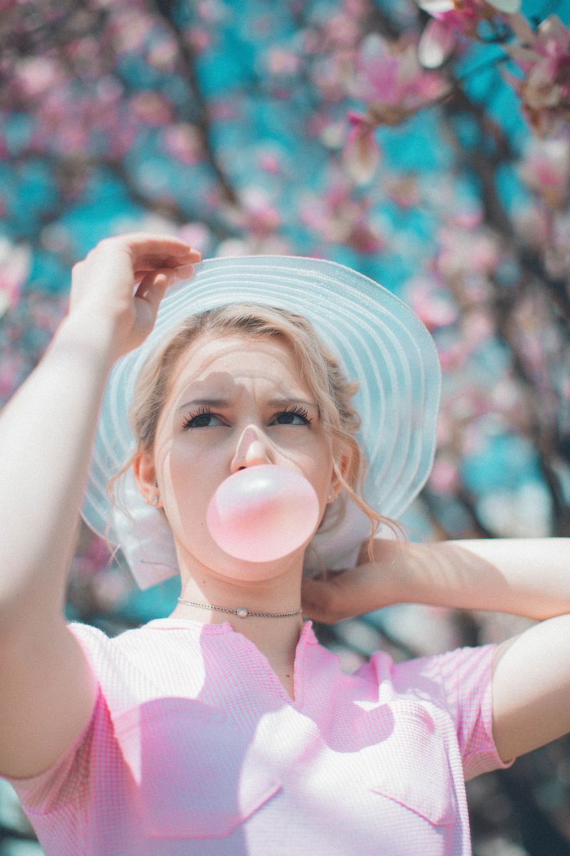 woman under pink tree blowing chewing gum
