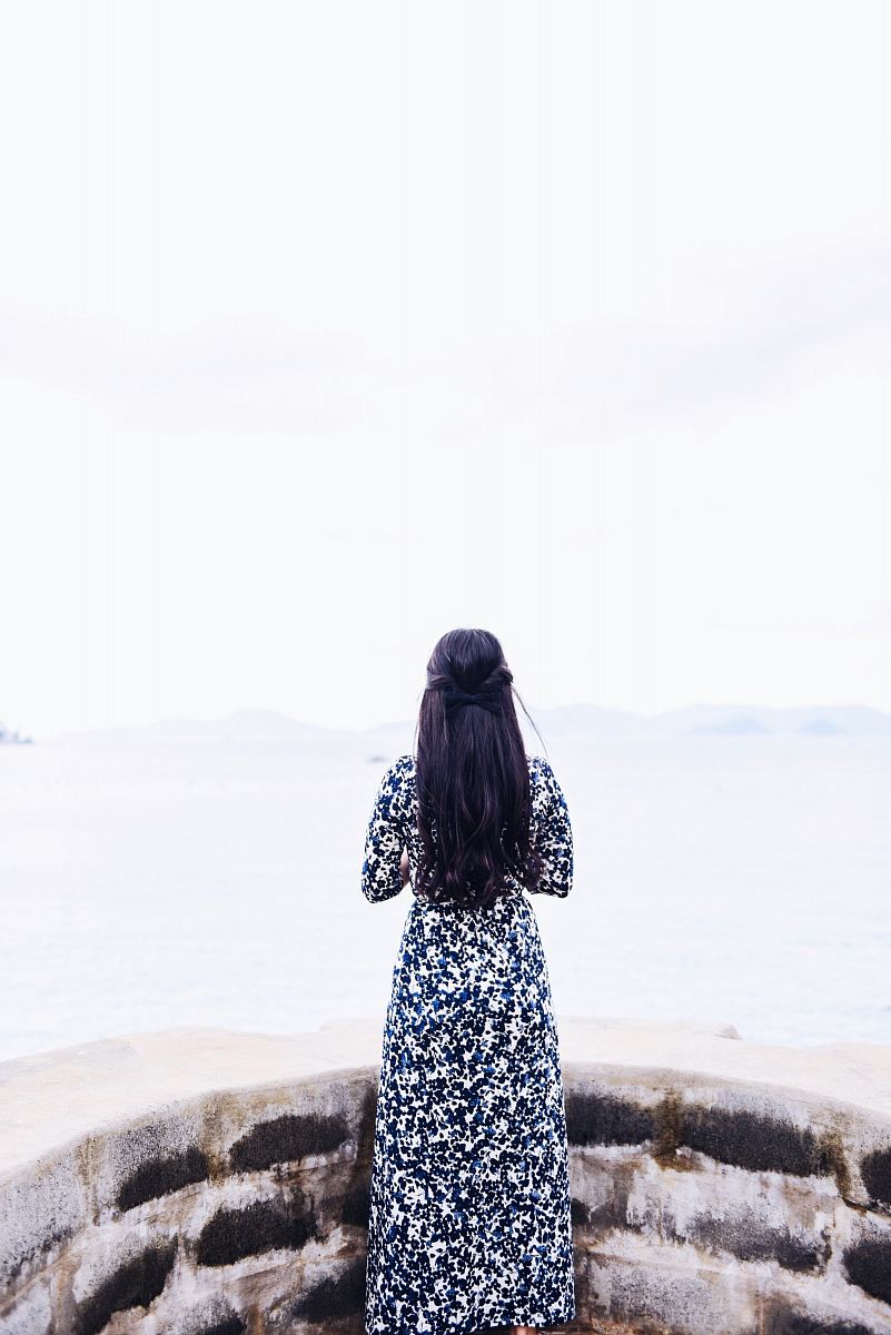woman wearing black and white long sleeve dress standing facing sea during daytime