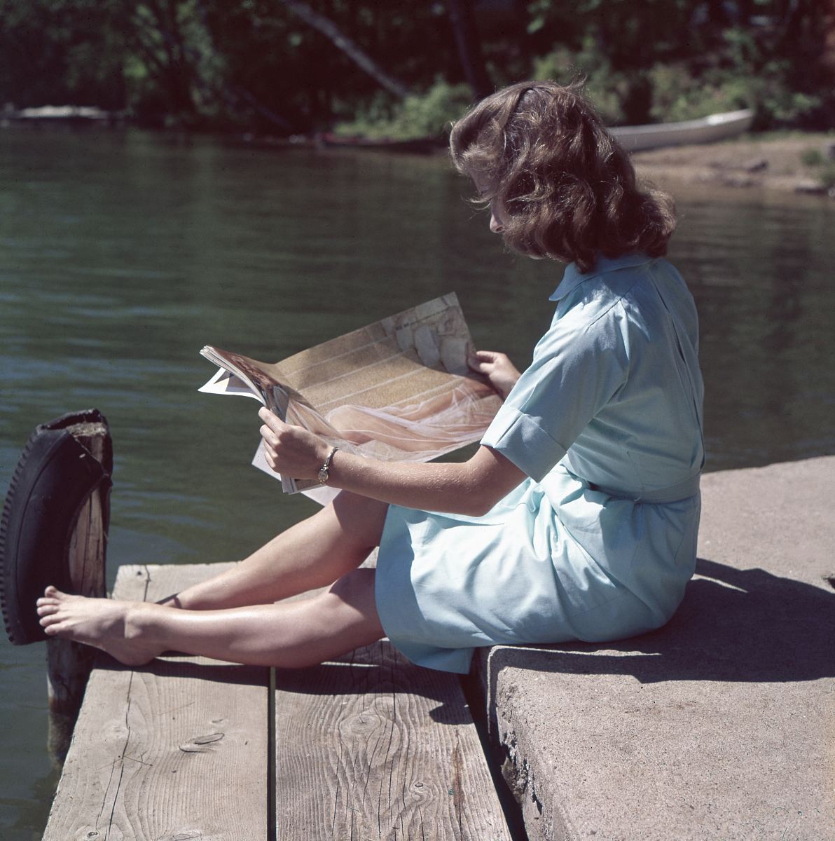 woman wearing blue dress reading magazine near body of water during daytime