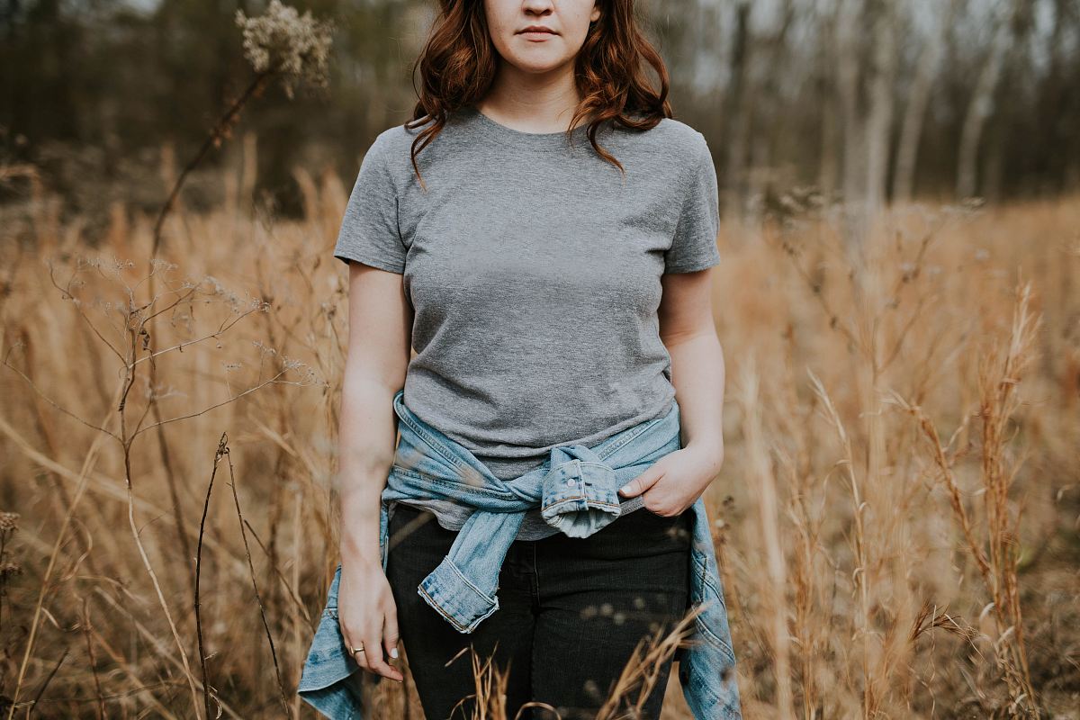 woman wearing gray crew-neck t-shirt with jacket wrap around her waist standing on brown grass field during daytime