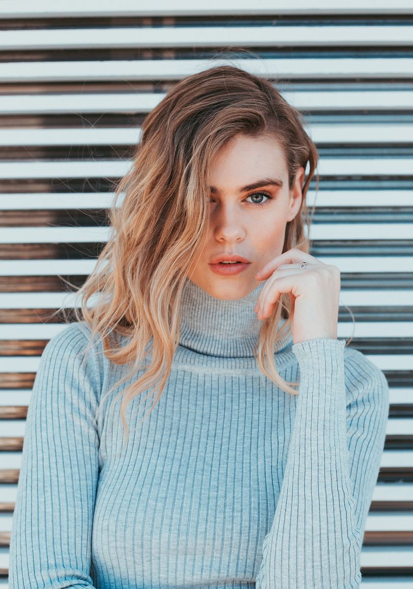 woman wearing gray turtle-neck top standing near white wall