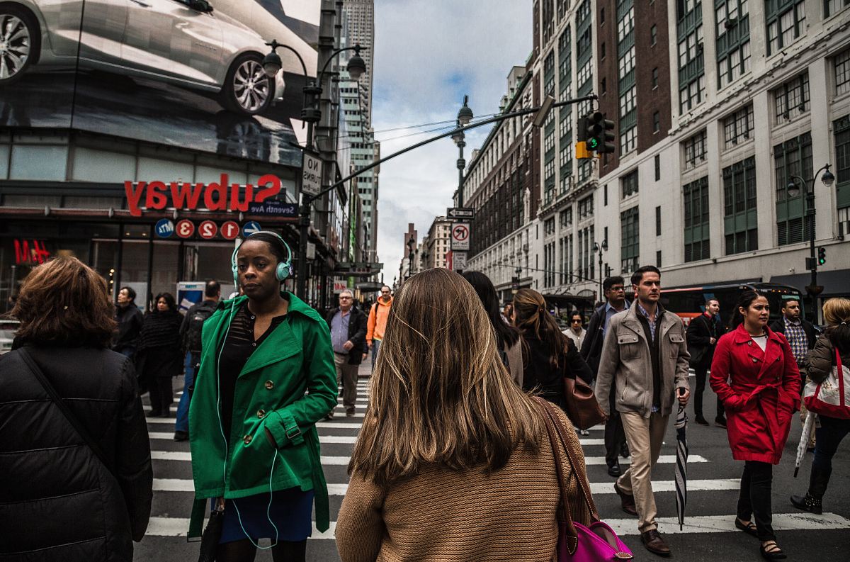 woman wearing green jacket walking on the pedestrian lane during daytime