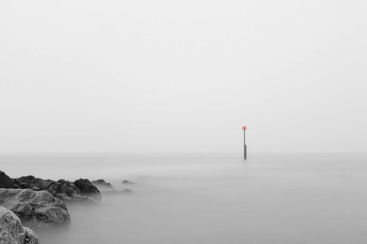 grey photo of pillar bouy on body of water rocks