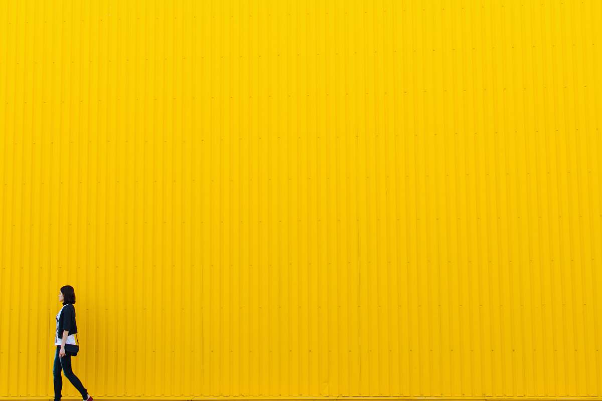 grey woman wearing black top standing near yellow wall brown