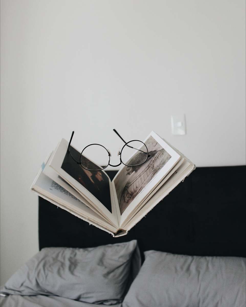 read black framed eyeglasses between opened book bed
