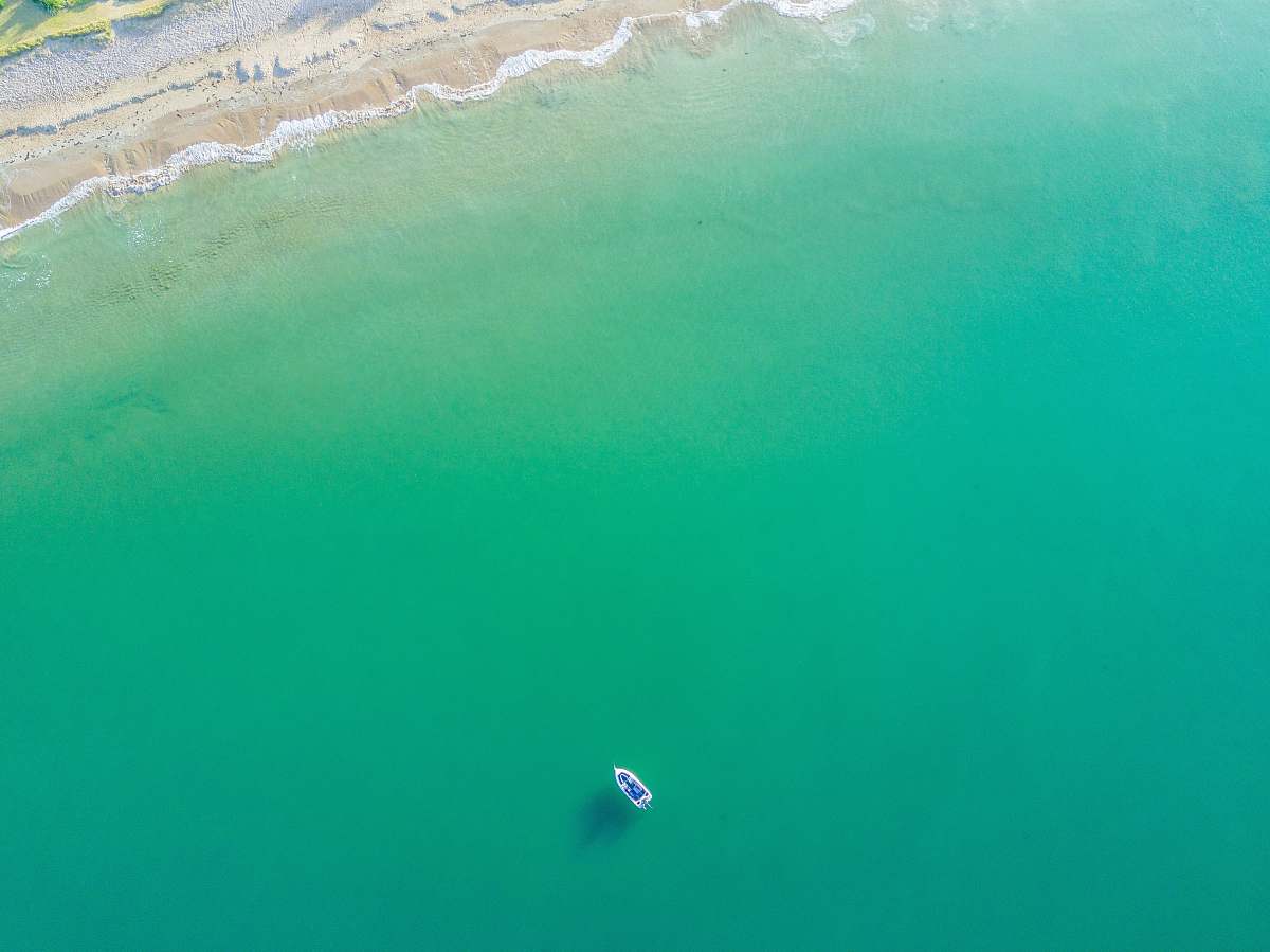 ocean aerial photography of white boat on green ocean near seashore sea