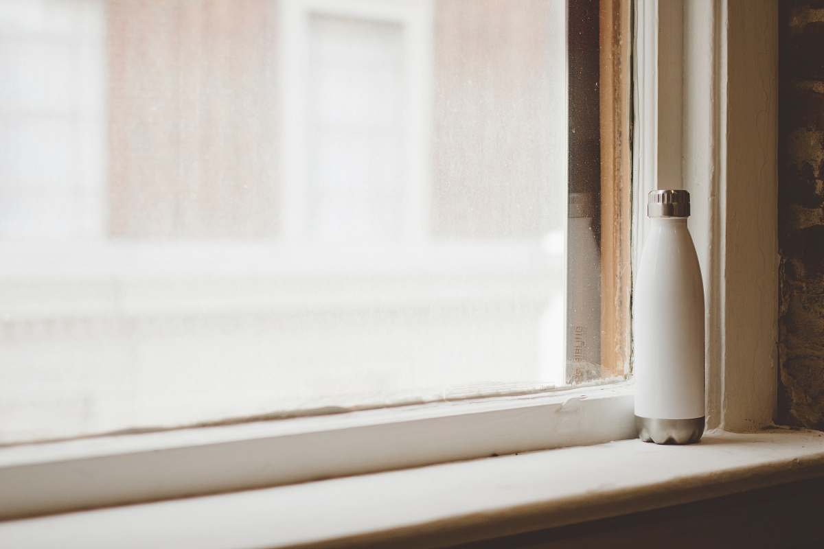 white gray and white vacuum flask beside window frame window sill