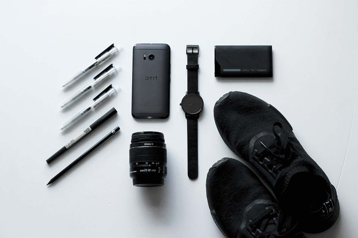wallet black HTC Android smartphone beside camera lens, ballpoint pens, and lace-up shoes electrical device