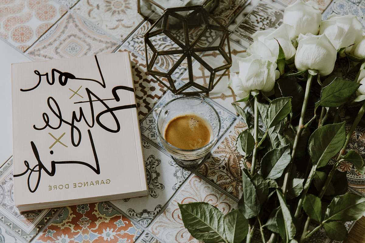 book clear glass cup filled with coffee near white roses and book jar