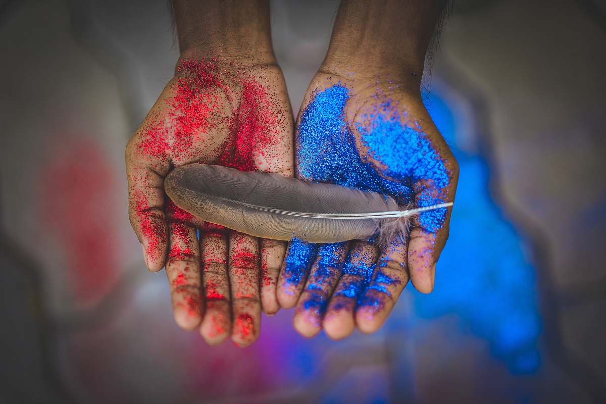 light top view photography of brown feather on blue and red painted hands feather