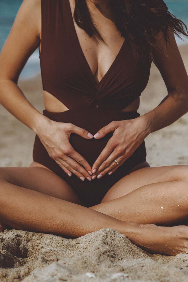human woman in black one piece swimsuit sitting on sand during daytime patient