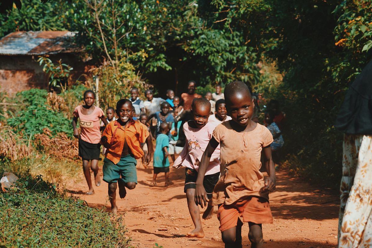children running and walking on brown sand surrounded with trees during daytime