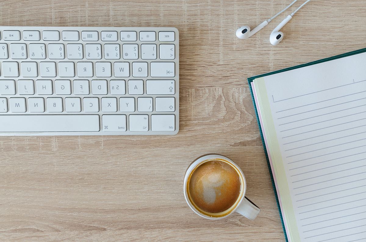 coffee latte near white wireless keyboard and Apple EarPods on the table photography