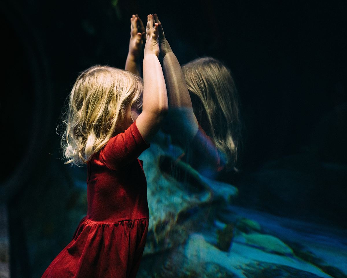 girl leaning on glass fish tank raising her two hands