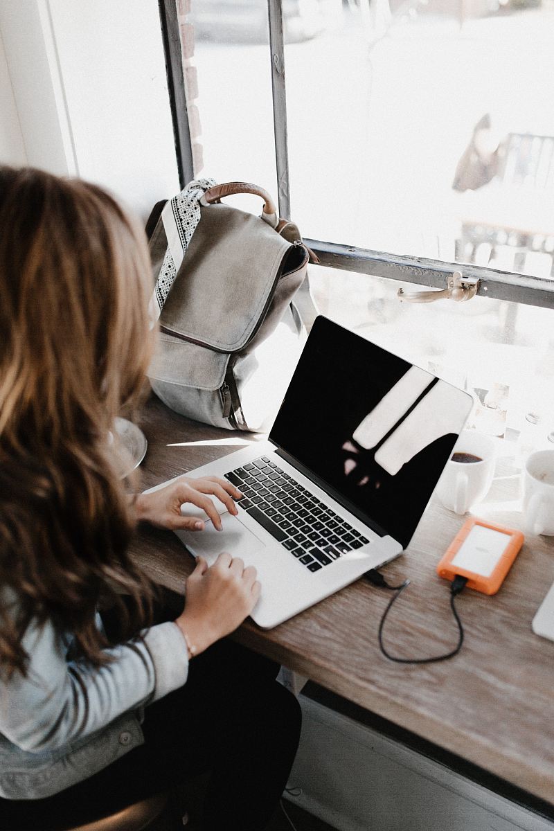 girl wearing grey long-sleeved shirt using MacBook Pro on brown wooden table
