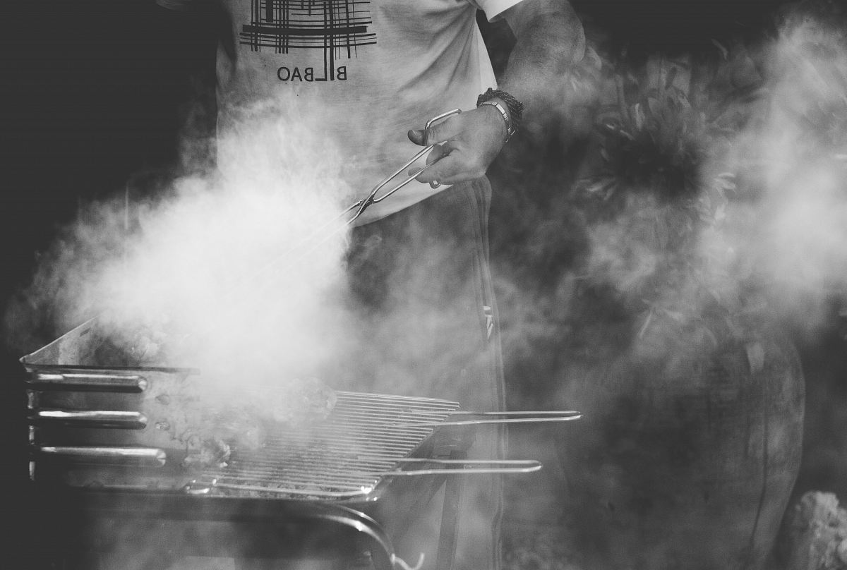 grayscale photo of man standing near gas grill