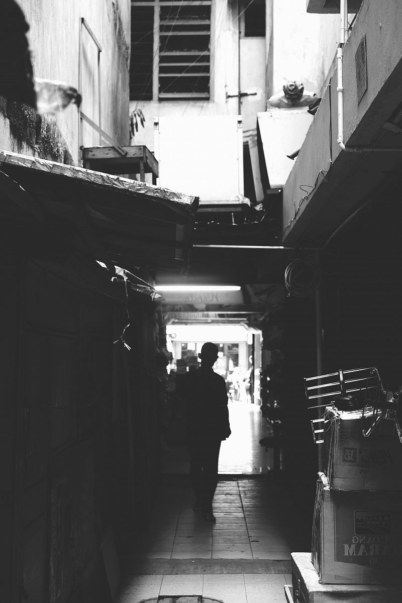 grayscale photo of man standing on pathway between houses