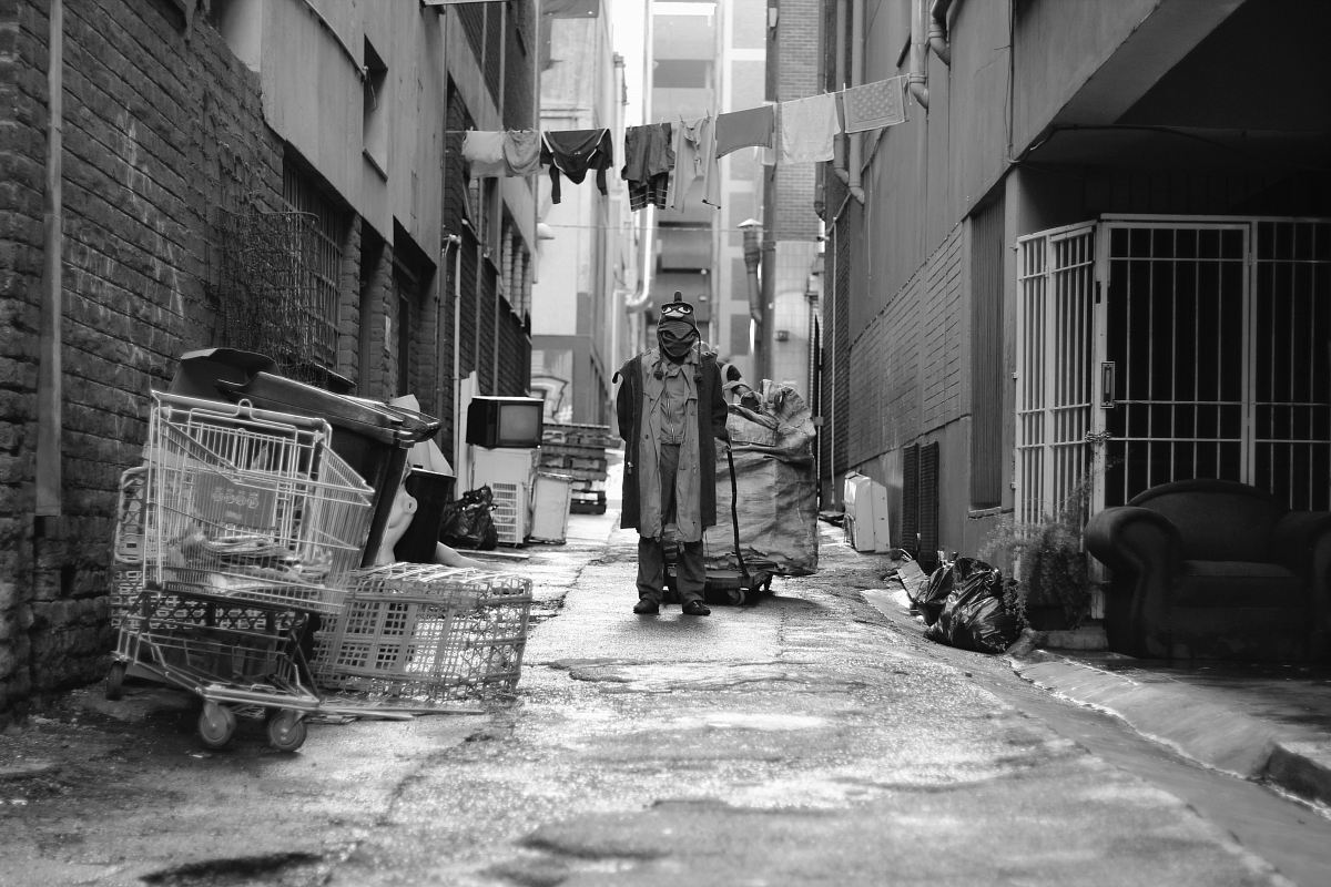 grayscale photography of man pulling cart in the middle of road