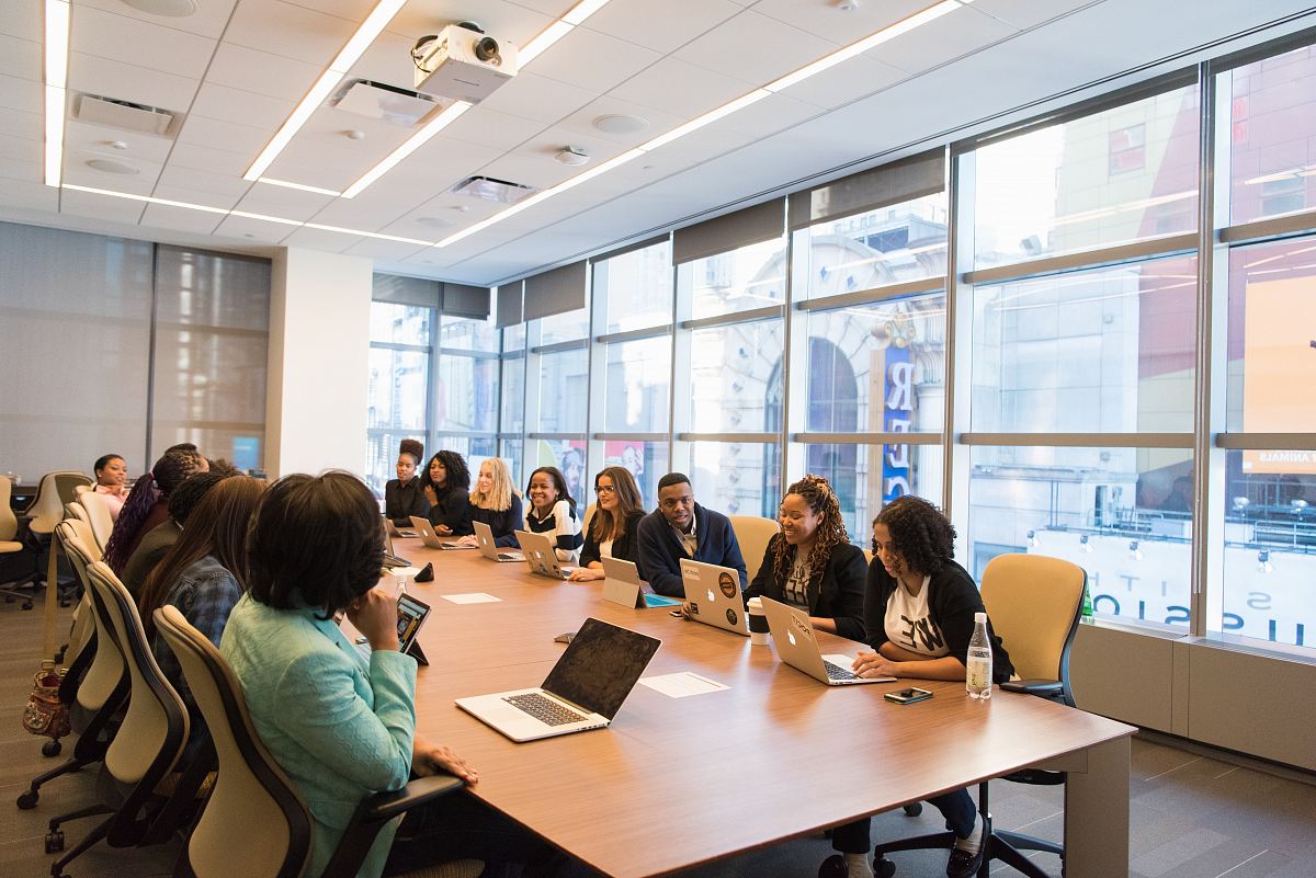 group of people sitting beside rectangular wooden table with laptops