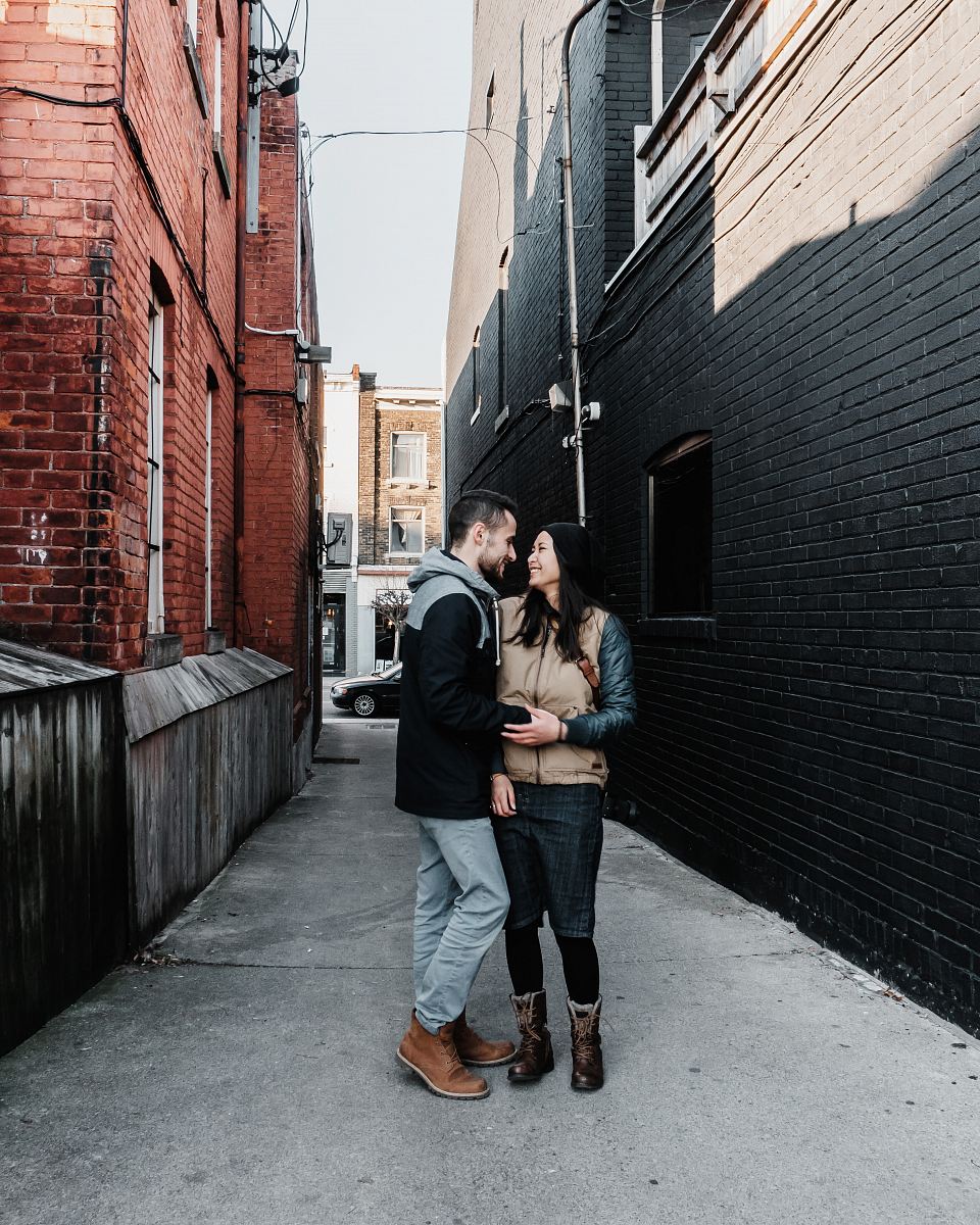 Capture the essence of love with this beautiful image of an engaged couple sharing a tender kiss in a charming downtown alleyway. Surrounded by urban architecture, this scene perfectly blends romance and city life, making it ideal for wedding planners, engagement announcements, or romantic-themed projects. The intimate moment symbolizes love's strength amidst the hustle and bustle of city living.