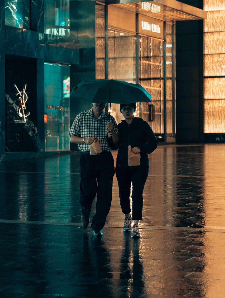man and woman under same umbrella walking while holding paper bags