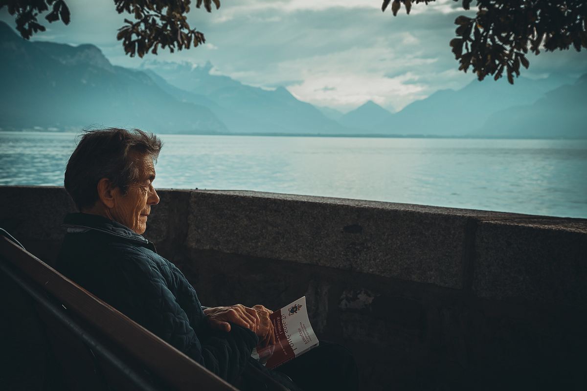 man sitting while holding a book watching on body of water